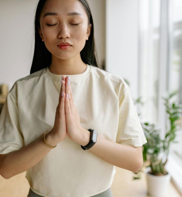 Woman meditating peacefully in a sunlit room with plants.